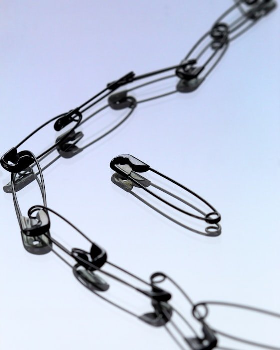 A chain of interlinked safety pins, with one pin lying open beside it