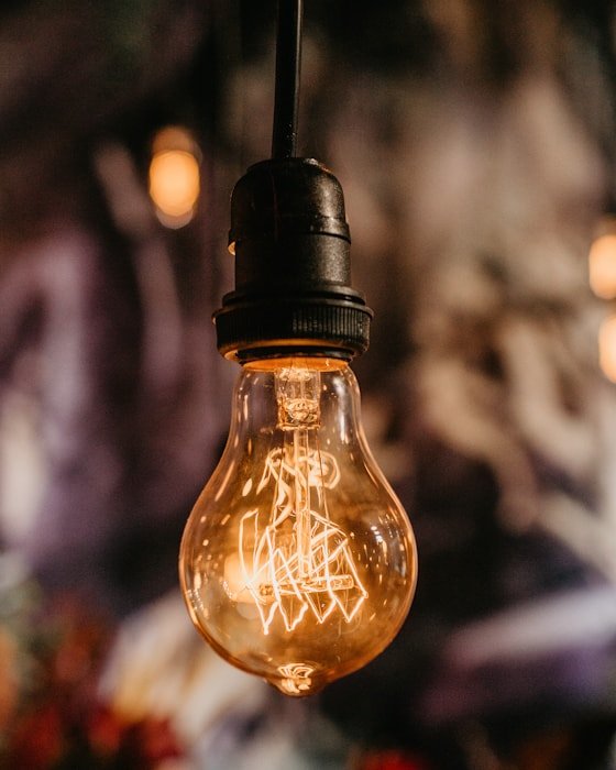 A glowing filament light bulb hanging against a warm, softly blurred background