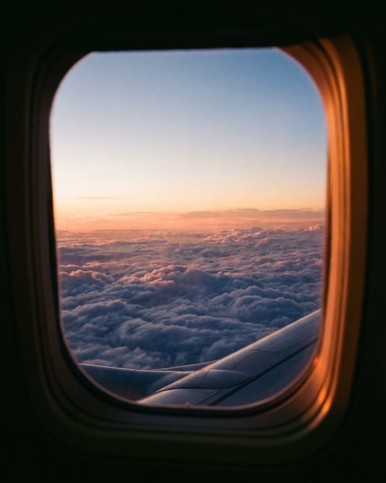 A view of a sunset over a sea of clouds through an airplane window