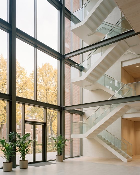 A light-filled modern stairwell behind a glazed façade, trees visible outside